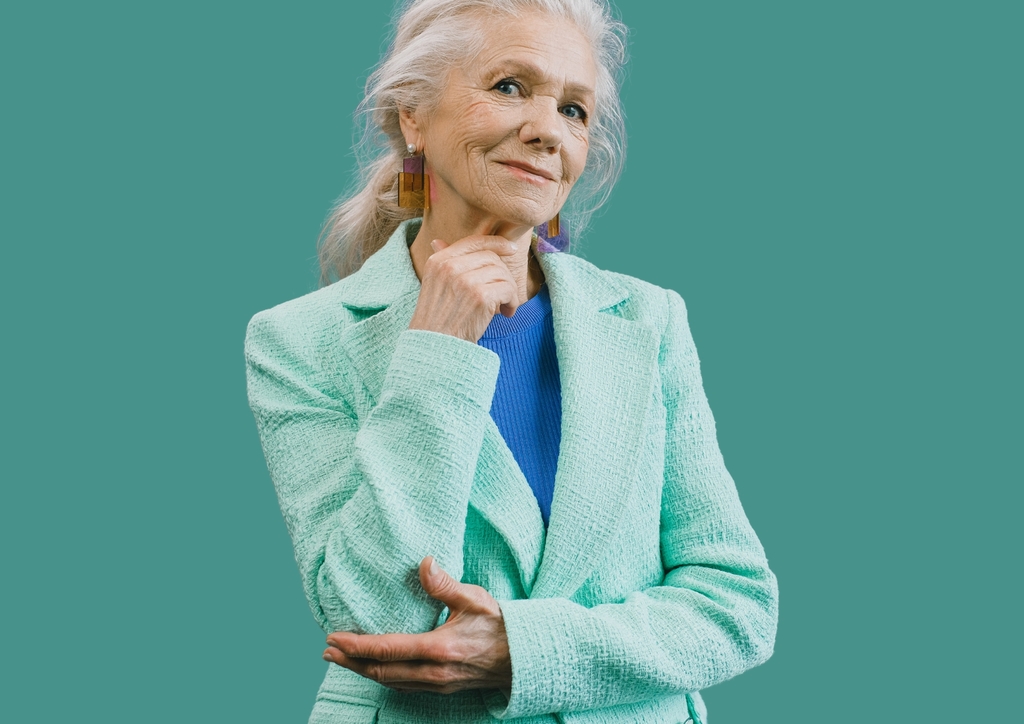 Elderly woman with long white hair pulled back, wearing colorful geometric earrings, a blue top, and a light teal textured blazer that exudes dignity. Her right hand gently touches her chin while her left arm is crossed at the waist against a solid teal background reminiscent of Hervey Bay's serene waters. Elderly woman with long white hair pulled back, wearing colorful geometric earrings, a blue top, and a light teal textured blazer that exudes dignity. Her right hand gently touches her chin while her left arm is crossed at the waist against a solid teal background reminiscent of Hervey Bay's serene waters.
